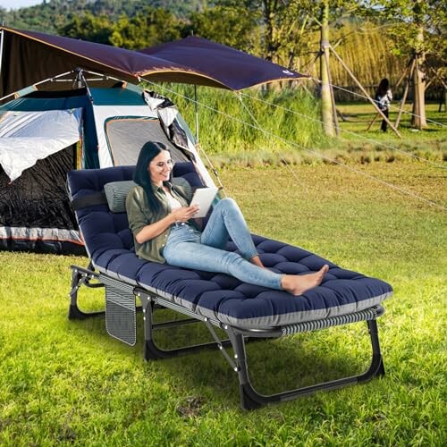 Frau liest auf einem Campingbett vor einem Zelt.